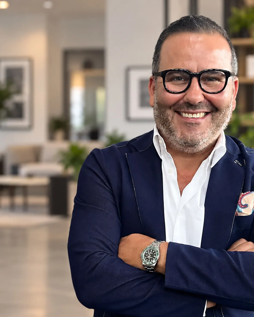 Mohammadi Akhabach, smiling with arms crossed, wearing a dark blue jacket and white shirt in a bright, modern open-plan office.